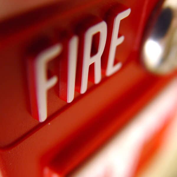 Close-up photograph of a red fire alarm pull station. The word 