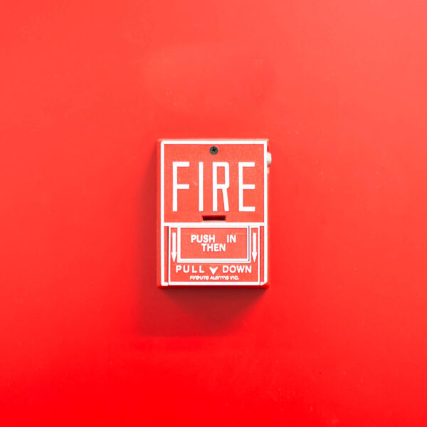 A red fire alarm pull station against a matching red wall. The alarm has text instructing to 