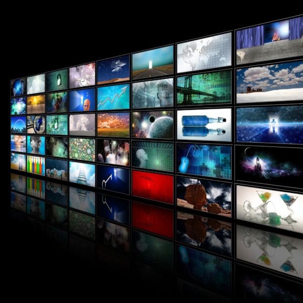 A tilted grid of numerous screens displaying a variety of colorful, vibrant images, including landscapes, abstract art, digital graphics, and nature scenes, all set against a black background with a reflective surface underneath, giving a sense of depth.
