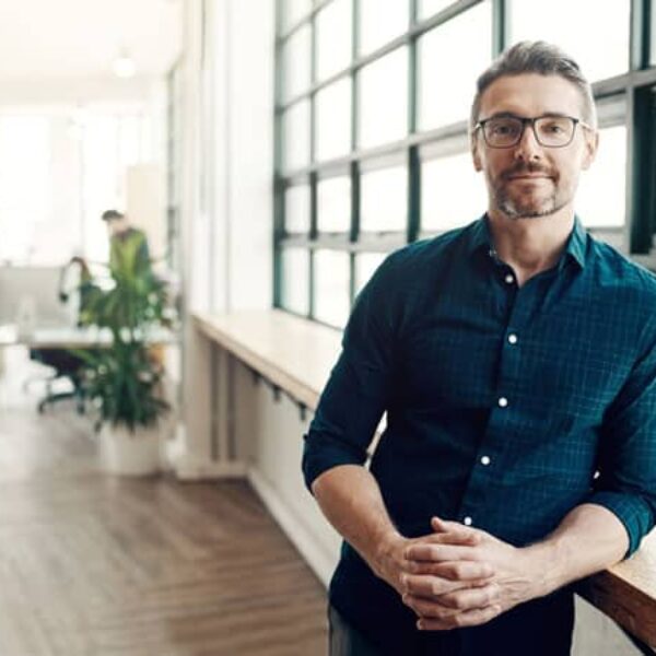 man dressed in business casual attire stands by a window